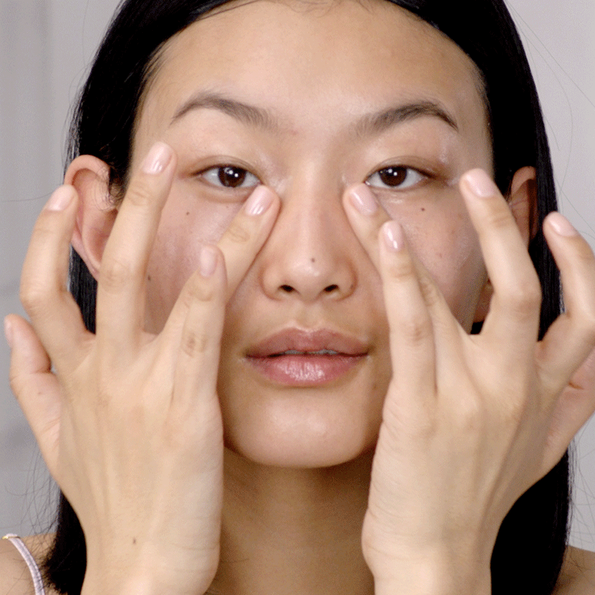 A light-tone model massaging an eye cream on her under-eye area to decrease puffiness. 